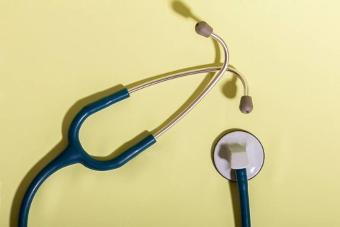 A medical stethoscope with a blue tube and gray earpieces is placed on a light yellow background,