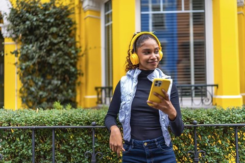Portrait of a cool african american woman listening to music using phone leaning on a rail next to