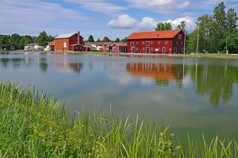 Red houses are reflected in calm water under a partly cloudy sky, Göta Canal, Götaleden, Västra
