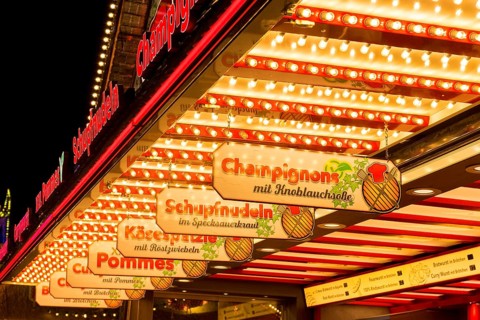 Illuminated market scene at night with signs for food: Mushrooms and cheese spaetzle, Cannstatter