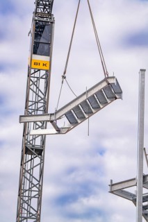 Close-up of a steel girder hanging from a crane on a construction site, staircase extension to the