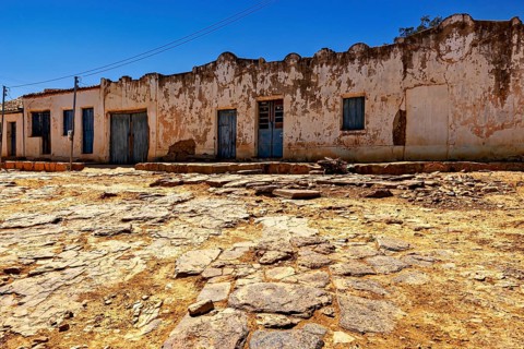 Dilapidated building with worn doors in front of an eroded road, settlement and villages in the