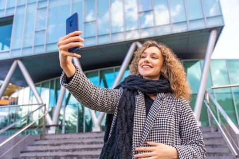 Beauty woman with warm clothes taking a selfie in the city during autumn next to a modern glass