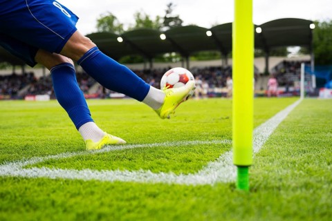 Football player taking a corner kick during a soccer match, striking the ball beside the corner
