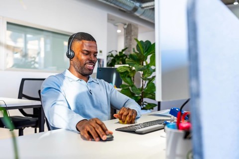 Young black man working at a computer while wearing a headset in a bright, modern coworking office,