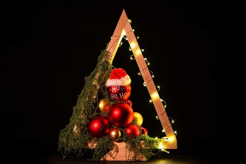 Modern DIY wooden Christmas tree with LED lights, moss, red balls and ornaments on a neutral