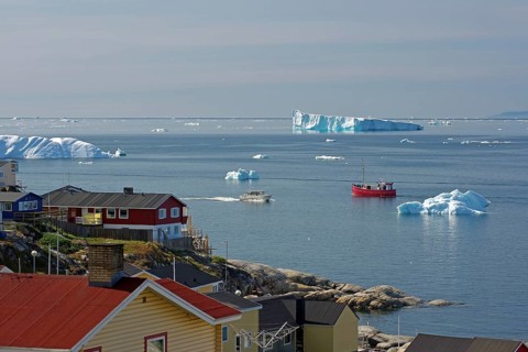 A quiet coastal town with boats in the sea and icebergs on the horizon, Arctic, Disco Bay,