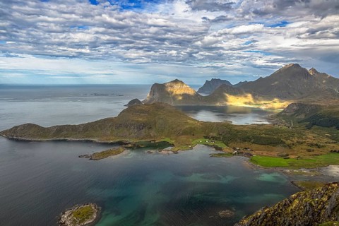 Dramatic aerial view of Lofoten coast with rugged mountains, turquoise sea and green landscape from