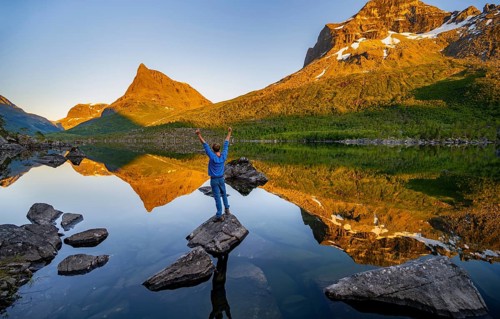 Young man standing on a rock in water, enjoying the landscape, picturesque mountain landscape with
