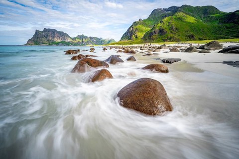Rocks on Uttakleiv sandy beach, coast and blue sea, long exposure, rocky mountain peaks,