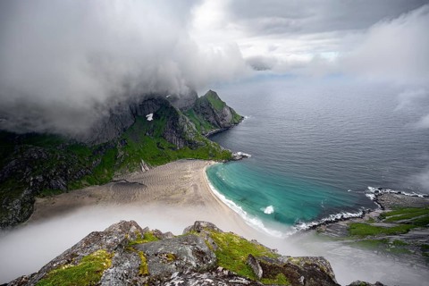 View from Helvetestinden summit, Bunesstranden sandy beach and blue sea, dramatic cloudy sky,