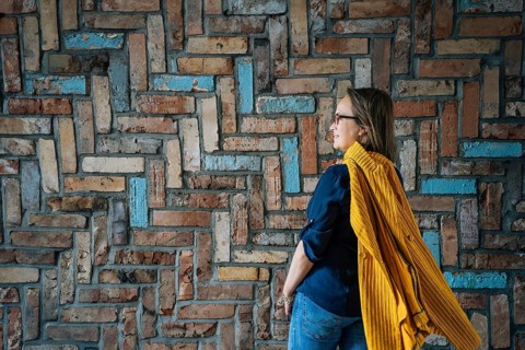 Side view of a 40-year-old woman in glasses against a colorful brick wall, Woman in casual attire