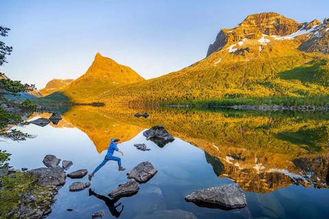 Young man jumping from stone to stone in water, picturesque mountain landscape in the Innerdalen