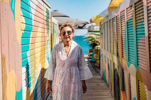 Senior Caucasian woman with glasses walks along a colorful boardwalk by the water. She wears a
