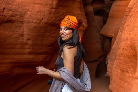 Woman tourist smiling and looking back while exploring wavy red sandstone formations and light