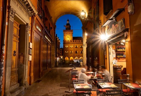 Restaurant in an illuminated alley in the evening, archway with Torre dell'Orologio in Piazza