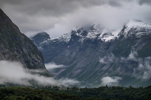 Freshly snow-covered mountain range above a valley and low-hanging scraps of clouds on the valley