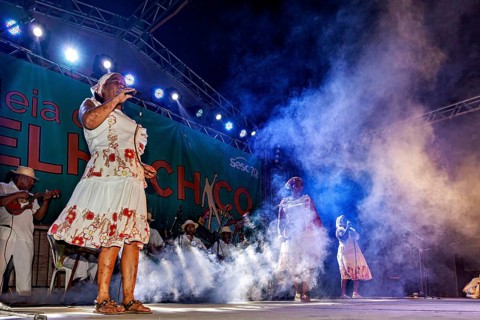 Singer on stage with microphone in atmospheric light and fog, a band plays and dances at a festival