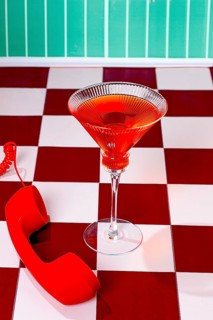 A glass filled with a red drink is placed on a table. A red phone sits beside the glass. The walls