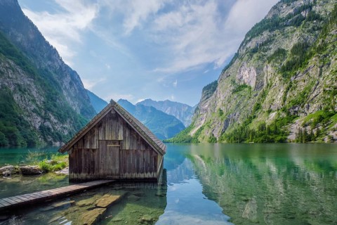 Wide shot of a wooden boat shed on the calm Obersee lake under a blue sky with soft clouds,