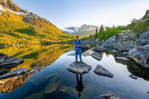 Young man standing on a rock in water, enjoying the landscape, picturesque mountain scenery in the