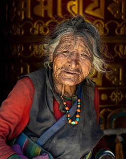 Very old woman with coral and turquoise necklace in traditional clothing in front of giant Buddhist