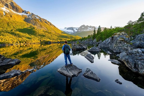 Young man standing on a rock in water, enjoying the landscape, picturesque mountain scenery in the