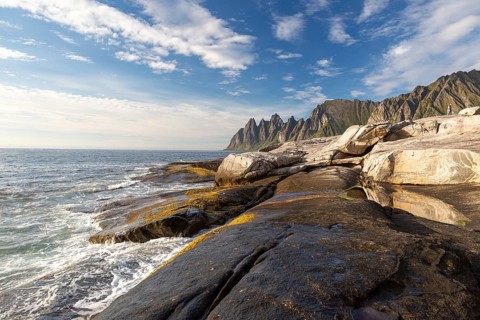 Waves hit the wet rocks of Tungeneset with the Okshornan Mountains in the background, Senja, Norway