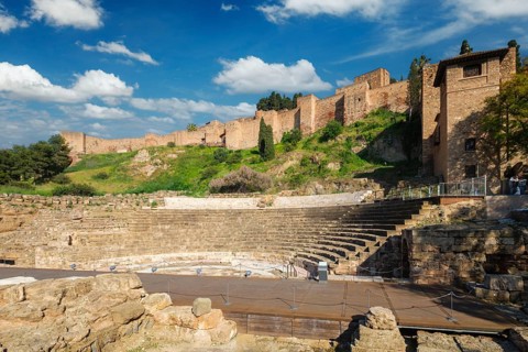 Scenic view of the Roman Theatre of Malaga and the Alcazaba walls across a green hillside, with