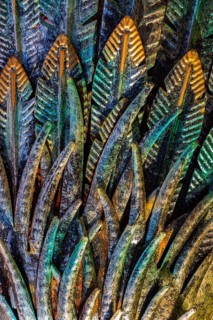Close-up of golden, greenish and turquoise painted carved metal feather details on ornamental