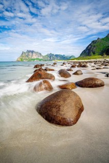 Rocks on Uttakleiv sandy beach, coast and blue sea, long exposure, rocky mountain peaks,