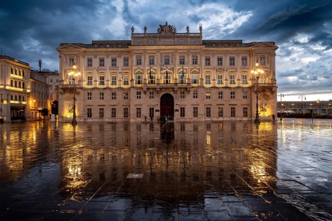 Illuminated square Piazza Unità d'Italia, Palazzo del Lloyd Triestino, with reflection, dramatic