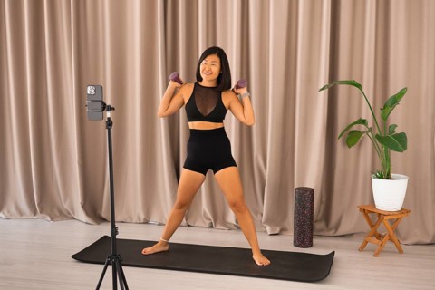 She is standing on a yoga mat with dumbbells, ready for a workout session