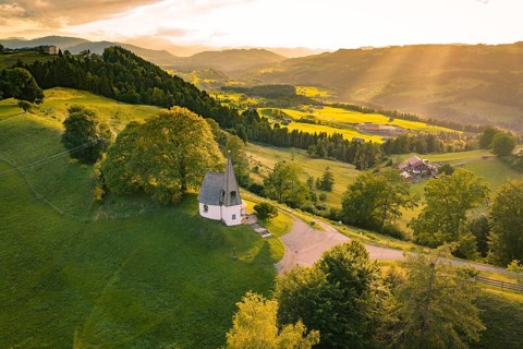 Idyllic hilly landscape with chapel and glowing evening sky, Bruder Klaus chapel, Allgäu, Bavaria,
