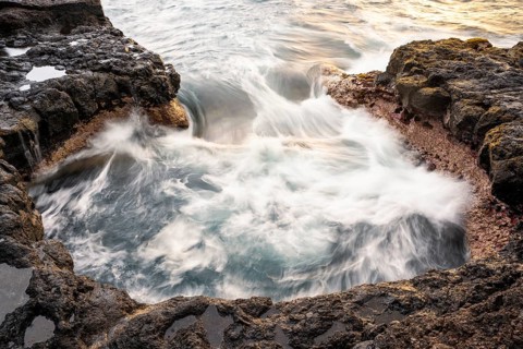 Seawater flows over lava rocks into a small pool. Long exposure, morning light. Coast near Puerto