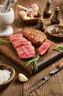 Beef steak sliced and arranged on wooden cutting board. Herbs, garlic and spices are placed around