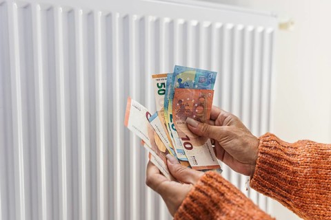 Woman holding euro banknotes and coins near home radiator during winter heating season in Europe.