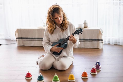 A woman on the floor playing a ukulele surrounded by colorful bells