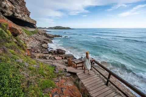 Young pretty woman wearing dress off coast and sea at Robberg Nature Reserve, Plettenberg Bay,