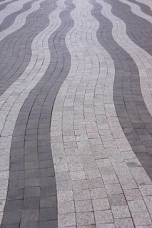 Curved lines of gray and white paving stones create an eye-catching pattern on an urban walkway.