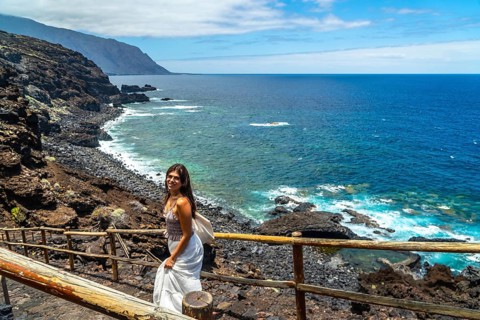 Woman standing on a wooden path along the rugged volcanic coastline of el hierro, immersing herself