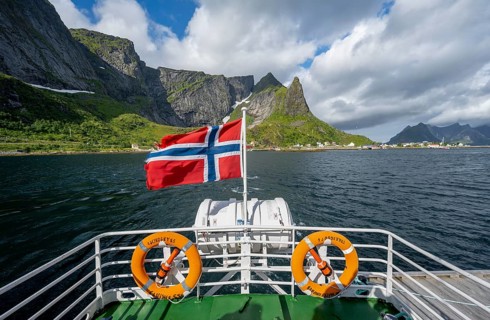 Boat trip on Reinefjord, Norwegian flag and fjord landscape with mountains, Lofoten, Norway