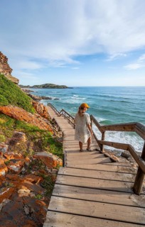 Young pretty woman wearing dress off coast and sea at Robberg Nature Reserve, Plettenberg Bay,