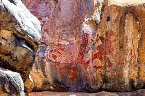 Red symbols and human figures on rough rock surface, prehistoric rock carvings in the thorny
