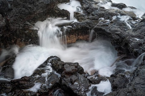 Seawater flows over lava rocks into a small pool. long exposure. Coast near Charco Azul, La Palma,