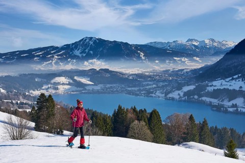 Sportive senior woman hiking with snow shoes in the snowy Allgaeu Alps above Lake Alosee,