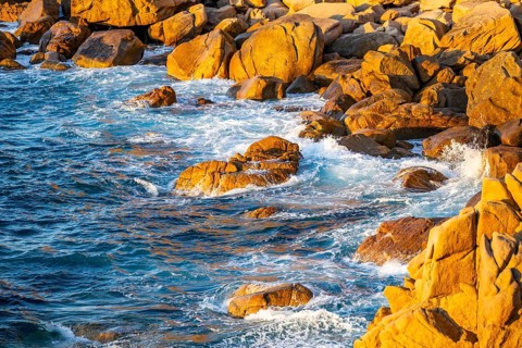 Surf at the coastline, blue water flows around the stones at Costa Paradiso in eveneing light,