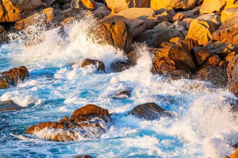 Surf at the coastline, blue water flows around the stones at Costa Paradiso in eveneing light,