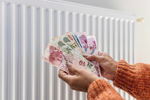 Woman holding Turkish lira banknotes near home radiator during winter heating season. Concept of