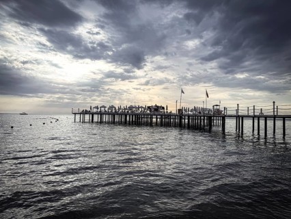 A long jetty with umbrellas stretches out into the calm sea under a dramatic sky, Side, Manavgat,